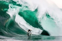 A surfer rides an enormous crashing wave.