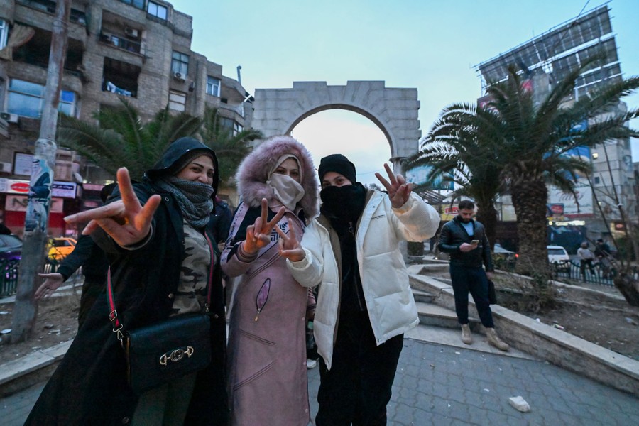 Several people pose together, making V signs, in a city square.