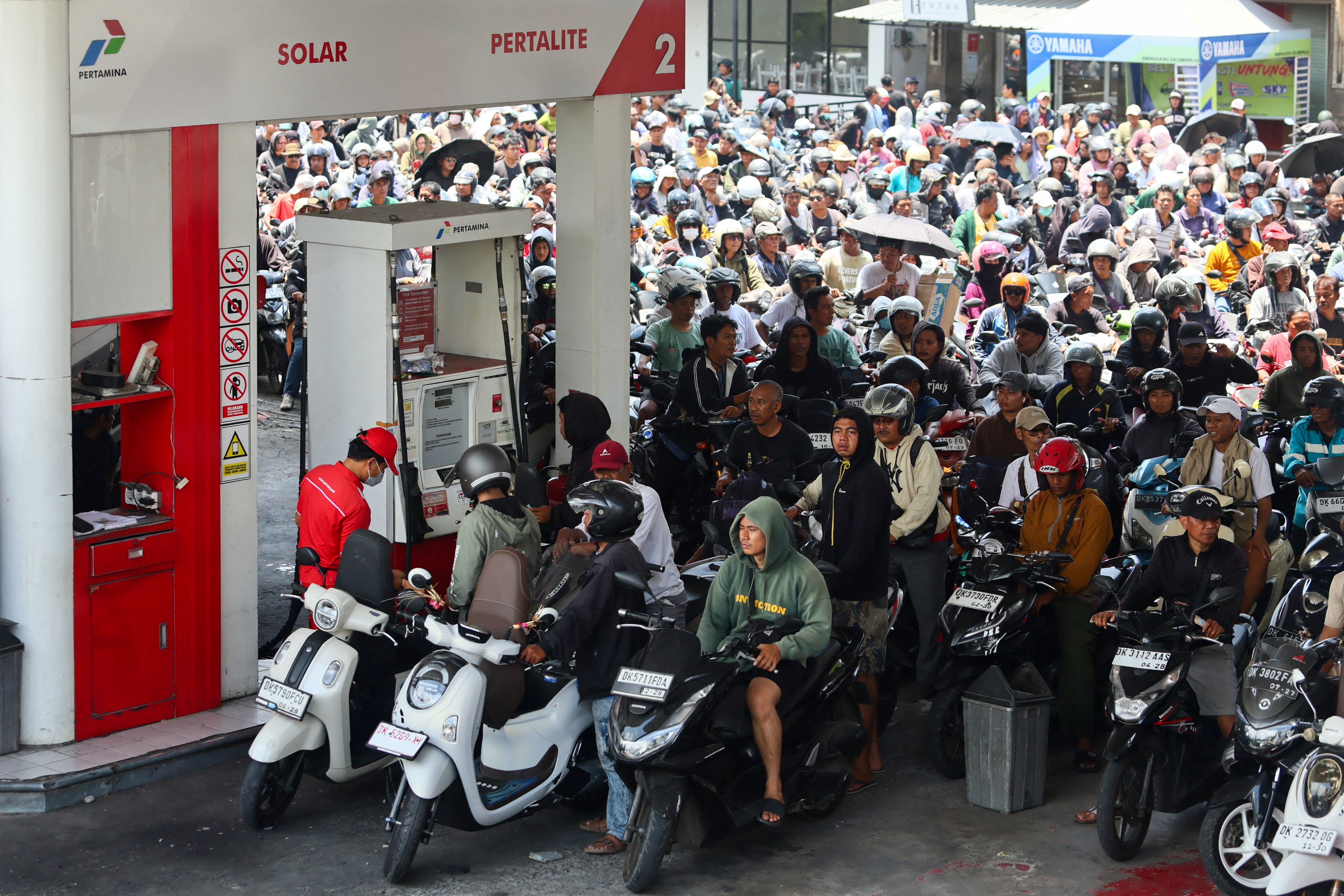 Many dozens of scooter and motorcycle riders jam into a queue at a gas station.