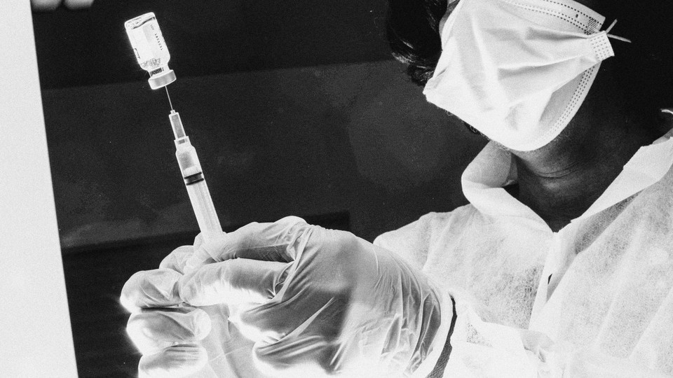 A nurse prepares a dose of vaccine in a syringe.