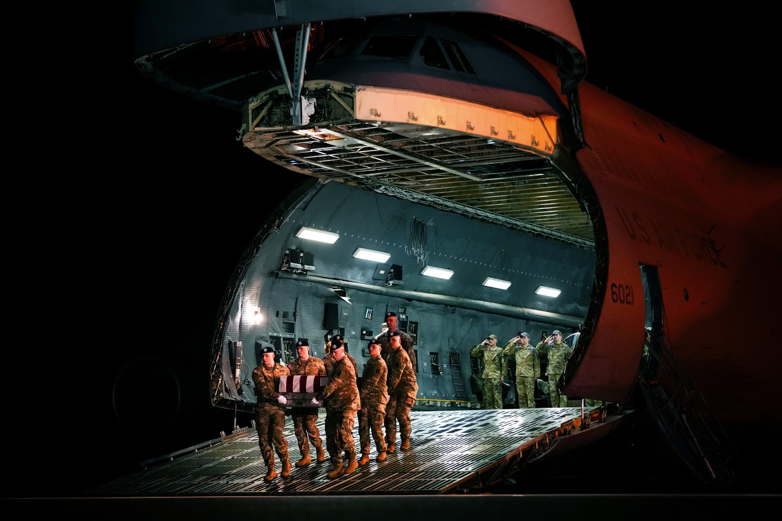 An Army carry team moves the flag-draped transfer case containing the remains of a U.S. Army soldier, walking down the ramp of a military aircraft.