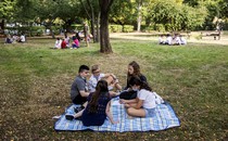 Groups of kids sit spread out on blankets in a park.