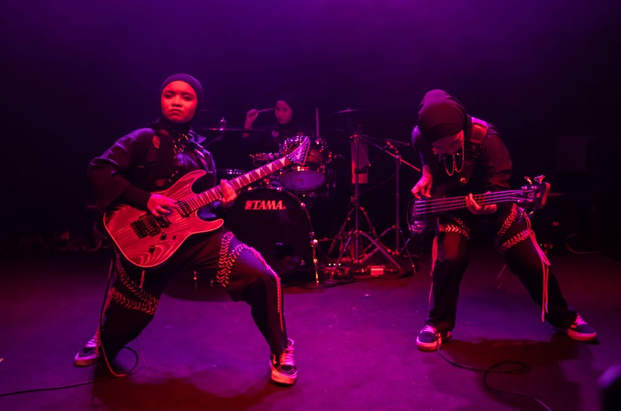 A trio of rock musicians performs on stage.