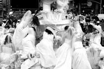 A black-and-white image of brides in wedding dresses scrambling onto a large structural wedding display