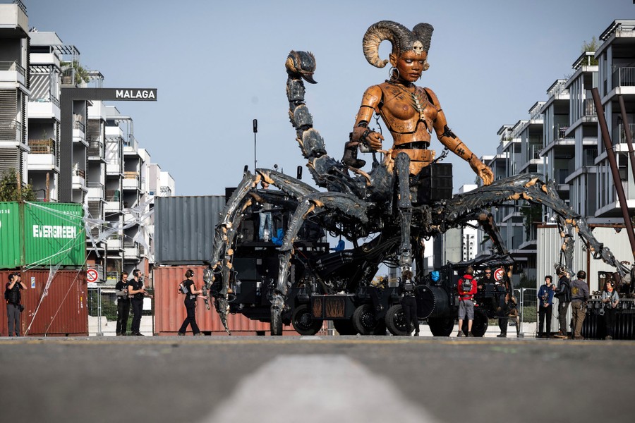 People operate a giant mechanical puppet, shaped like a mythical scorpion with the torso of a horned woman.