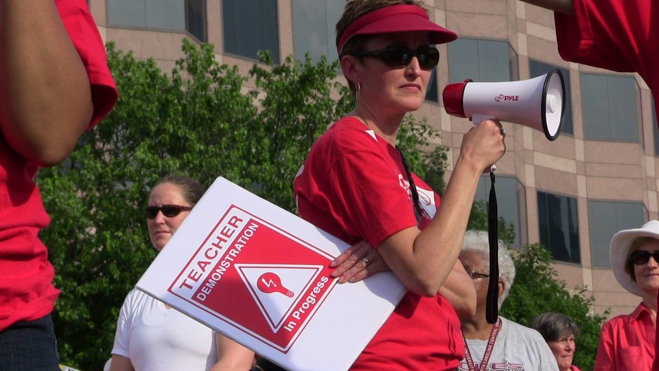 Angie Scioli holds a megaphone and a poster that reads "teacher demonstration in progress"