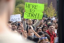 A protester holds a sign that reads "Here to Stay!" 