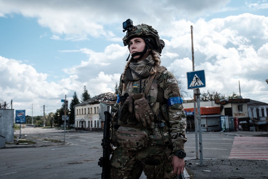 A Ukrainian soldier stands on a sidewalk in an abandoned street.