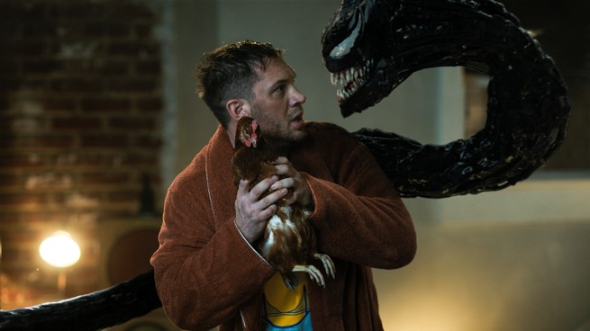 Eddie holds a chicken while Venom looms menacingly.