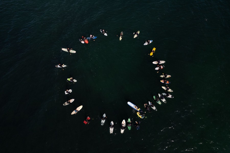 An overhead view of a circle of surfers floating in the ocean