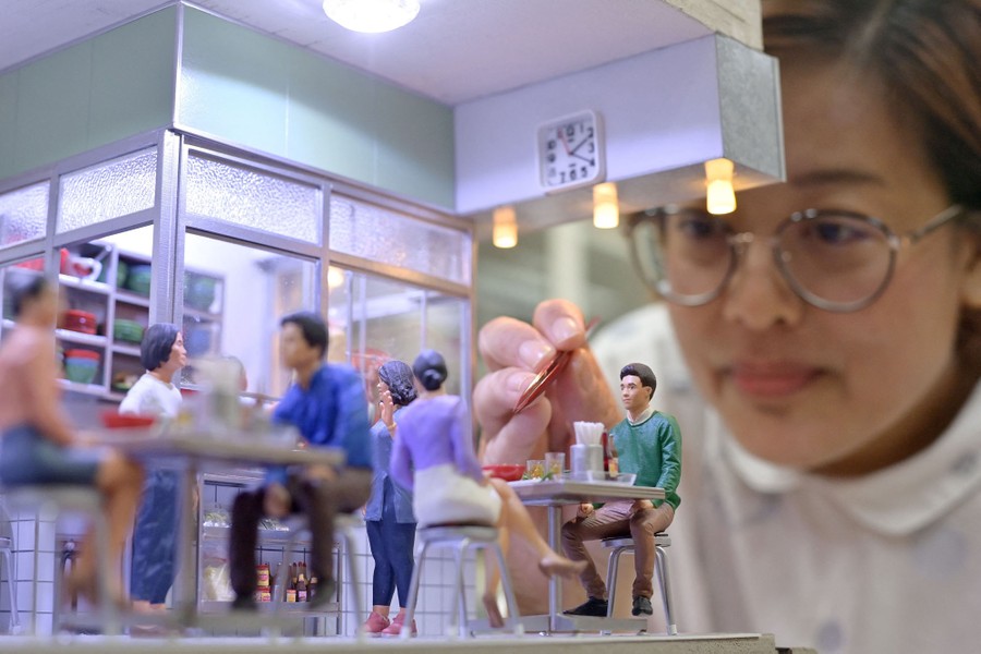 A person leans close to a small diorama of a restaurant.