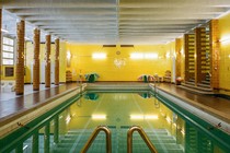A blue swimming pool in a yellow tiled room with brown tiled columns