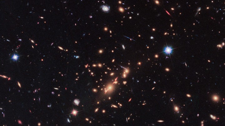 A Hubble Telescope image that includes a red, disk-shaped galaxy seen through a gravitational lens in the upper right corner.