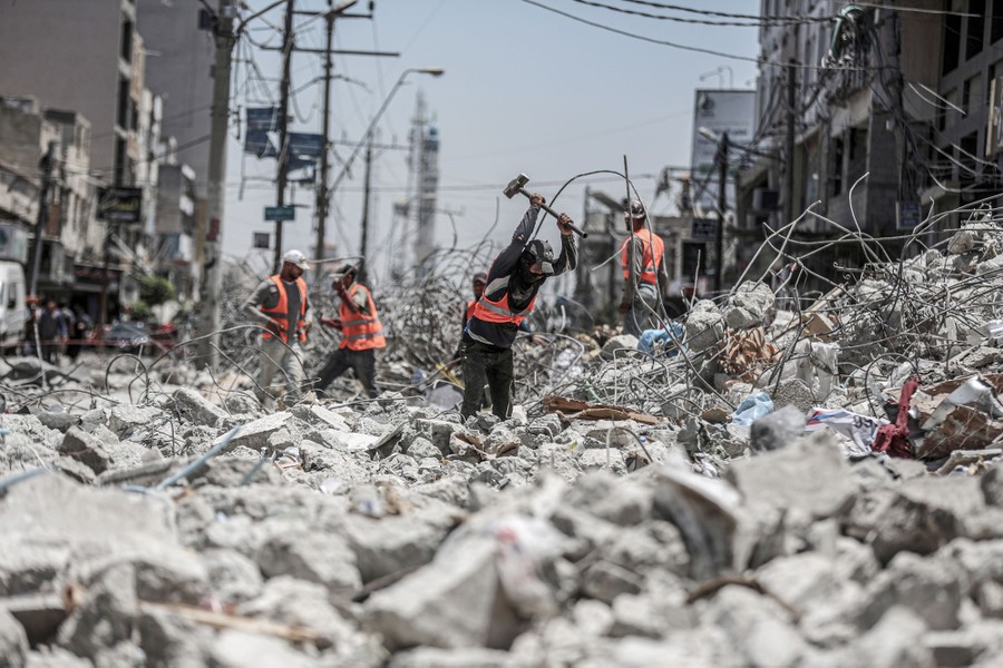 Several people in safety vests work in a pile of rubble in a street.