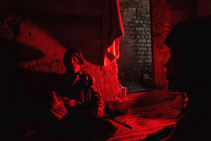 Several soldiers take cover in a brick structure lit by a red light.