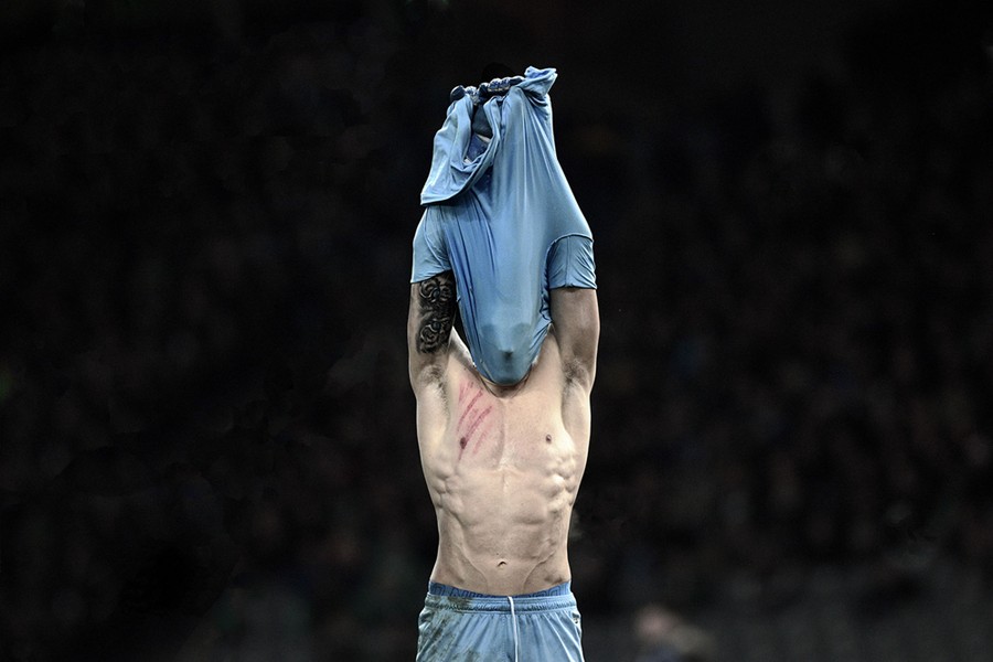 A goalkeeper pulls his shirt off, stretching the fabric over his face.