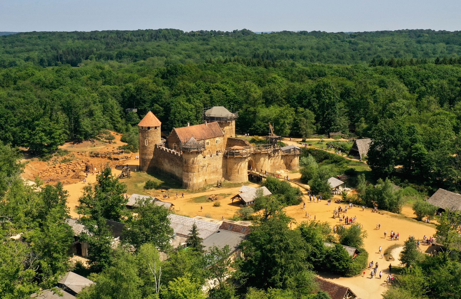 An aerial view of a small medieval-style castle in a wooded area.