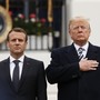 Macron standing with arms at sides next to Trump, who has a hand over his heart
