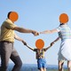 Two parents and one little kid hold hands in a circle, on a green field with a big blue sky in the background