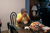 A woman sits at a table in her apartment, praying