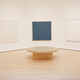 a white room with Agnes Martin's paintings on the wall and a round seat in the center