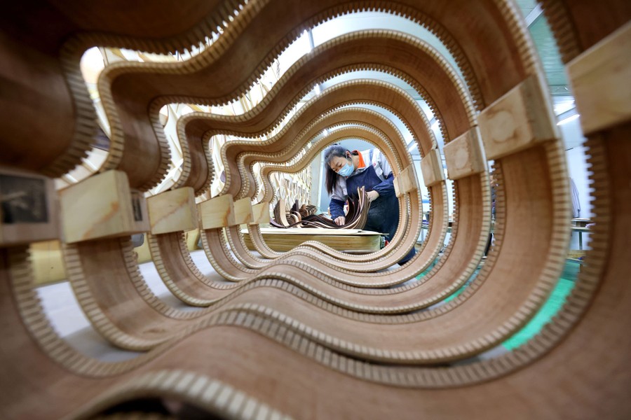 A worker builds a guitar, captured through the empty frames of six other partly assembled guitars.