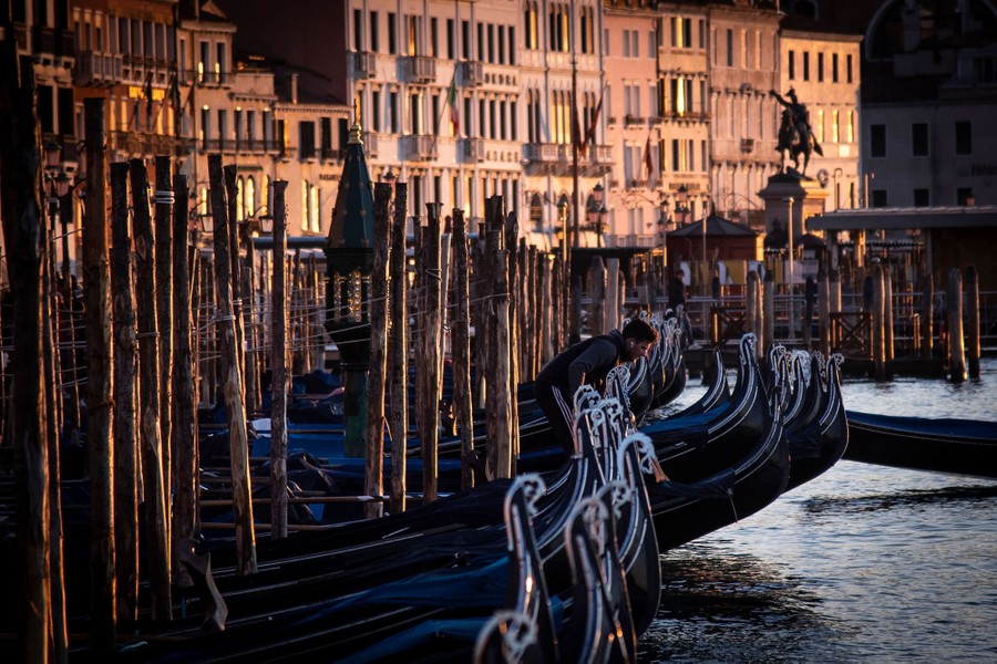 A man stands on a gondola moored in Venice.