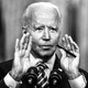 President Joe Biden speaks into a microphone with his hands held up to frame the lower half of his face.