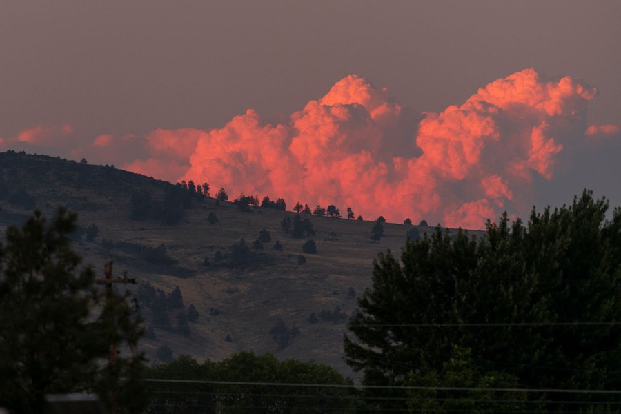 Thick clouds of smoke are seen in the distance above a hill.