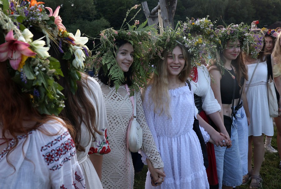 Women wearing floral wreaths hold hands and dance.