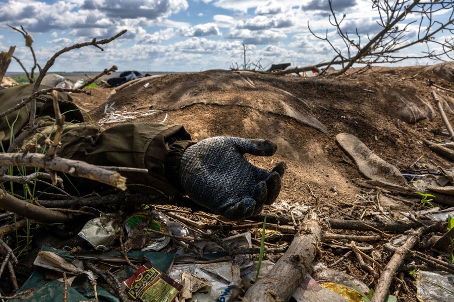 The gloved hand of a dead soldier is seen among broken branches and debris.