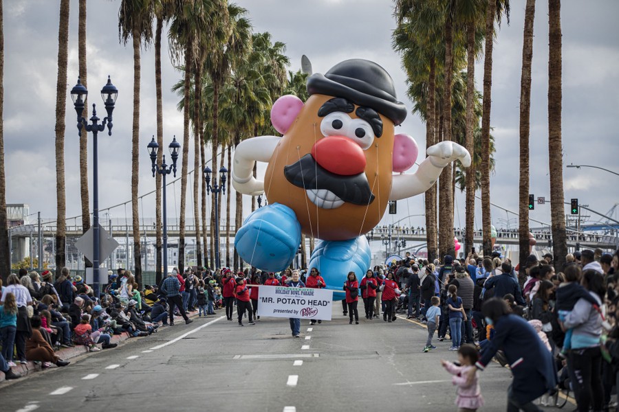 A Mr. Potato Head balloon in a parade, marching down a palm-tree-lined street