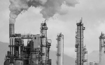 Smoke stacks at an oil refinery are shown against a gray sky