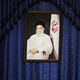 A portrait of Khamenei hangs against a blue curtain.