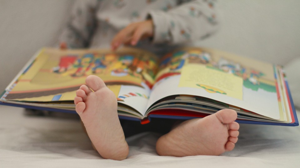 A small child reading a picture book on a bed
