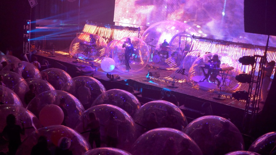 Durina a performance, band members onstage and audience members in front of them are encased in many clear plastic bubbles about 7 to 10 feet in diameter.