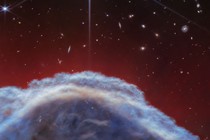 A space telescope image showing part of a cloud-like nebula with stars and galaxies visible in the background