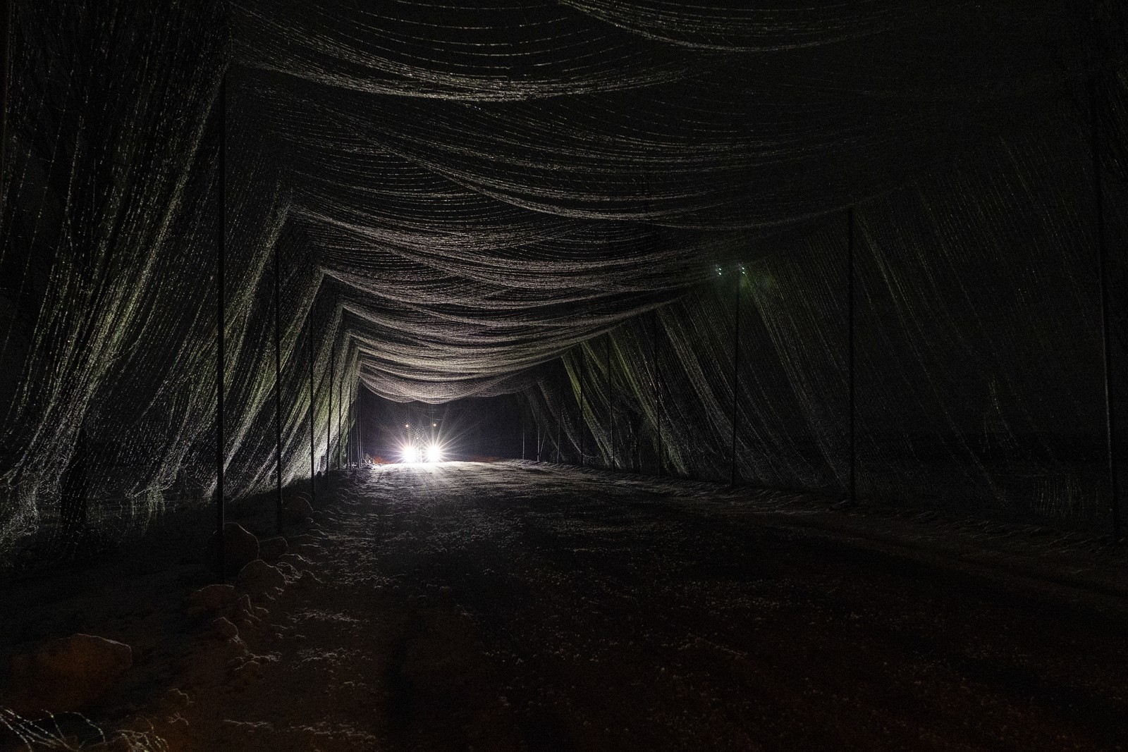 A vehicle travels at night along road section that has been covered with anti-drone netting.