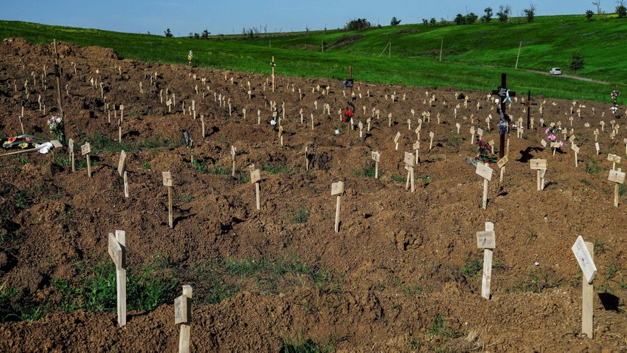 Rows of temporary grave markers stand in piles of dirt on a hillside.