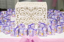 An ornate box sits on a table surrounded by small packages wrapped in floral paper and ribbon tied in a bow.