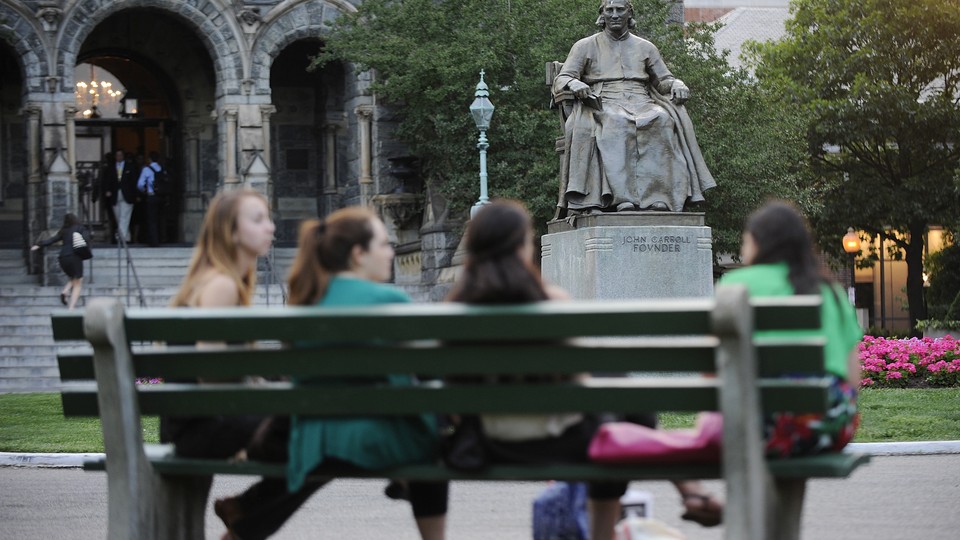 Students sit on a bench in front of a statute of the university founder John Carroll at Georgetown University.