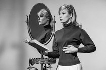 A woman stands next to a mirror reflecting her image