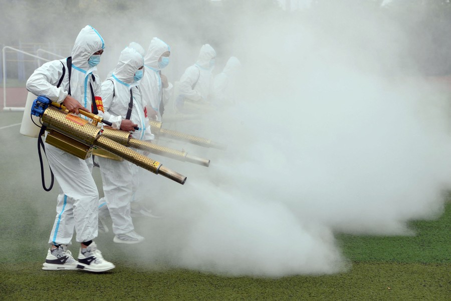 People wearing protective suits spray disinfectant on a playing field.