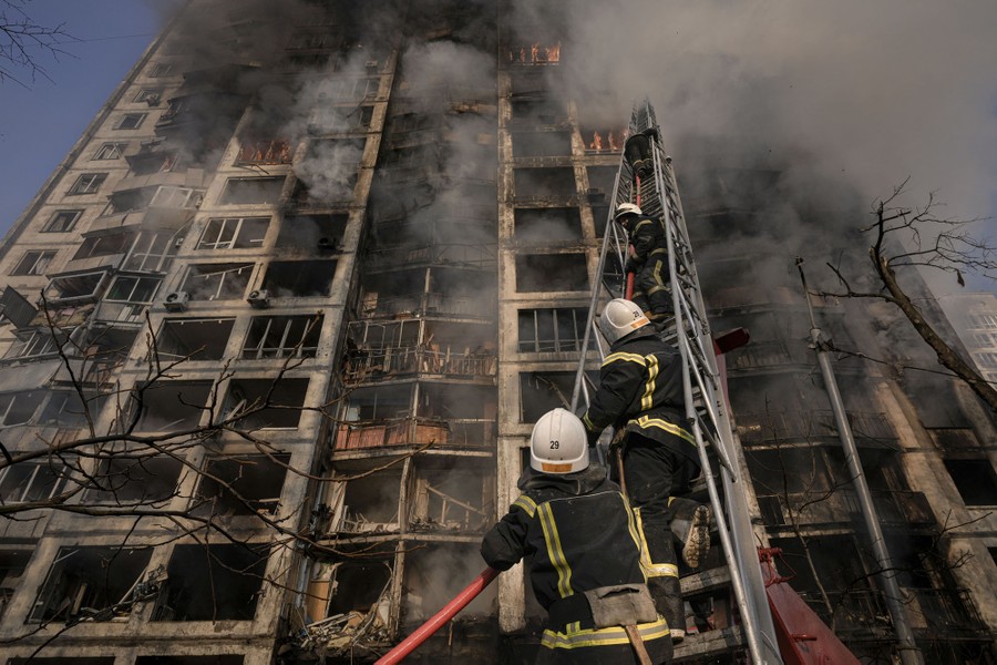 Firefighters climb a tall ladder while working to put out a fire in a high-rise apartment building.