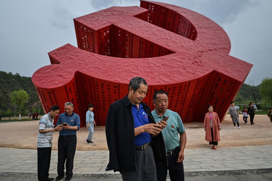 People stand together near a large monument shaped like the Communist hammer and sickle.