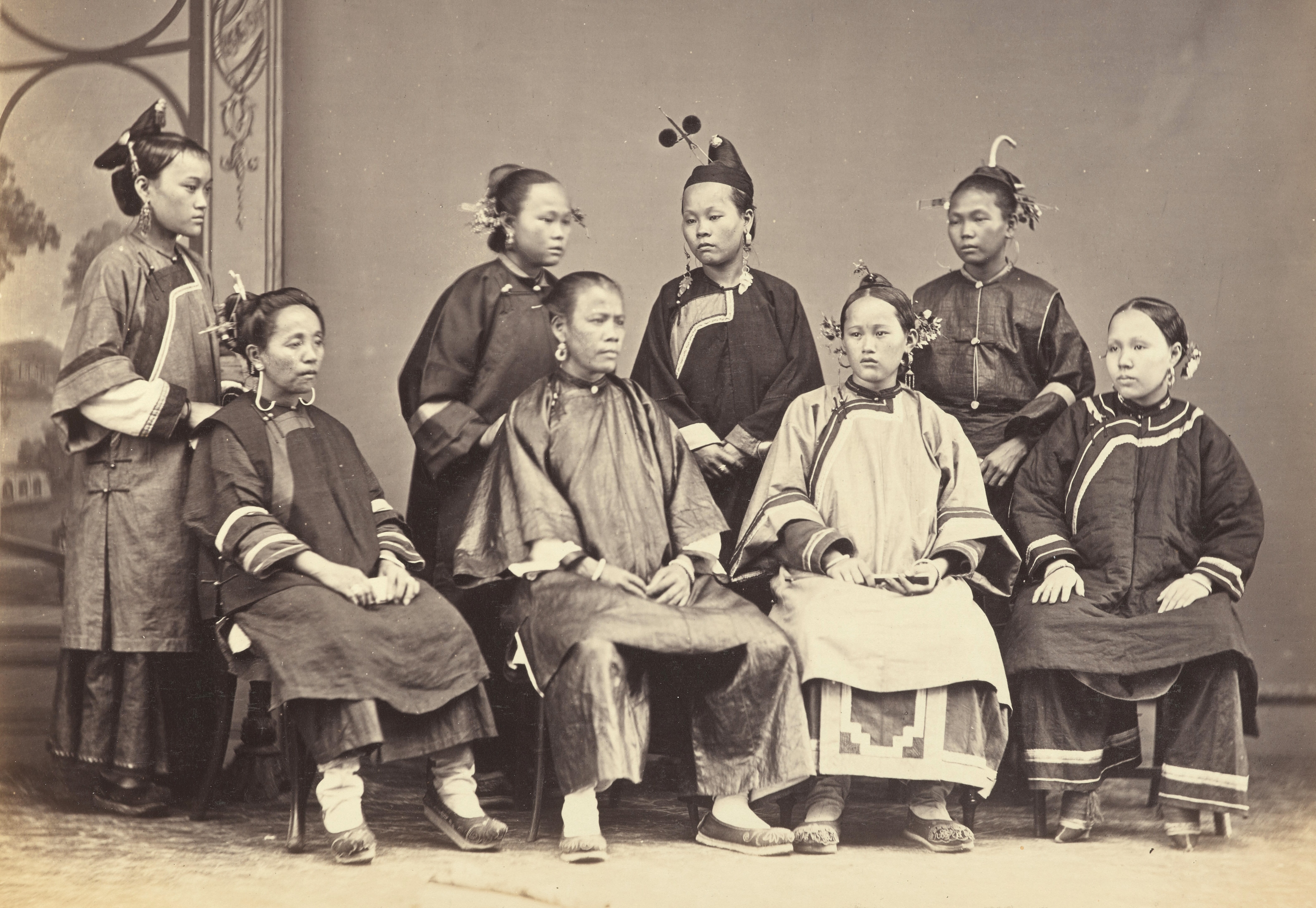 Eight women sit and stand, posing, while wearing traditional Chinese garments.