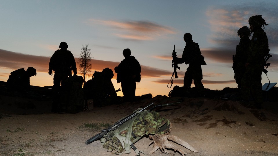 A photograph with camo gear and a rifle illuminated in the foreground and a half-dozen soldiers silhouetted in the background.