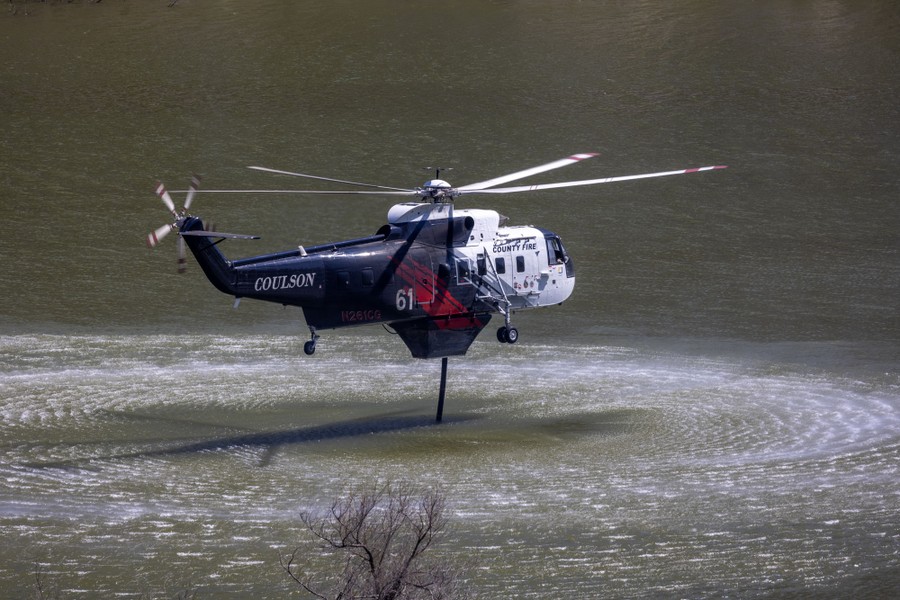 A firefighting helicopter refills while hovering above a body of water.