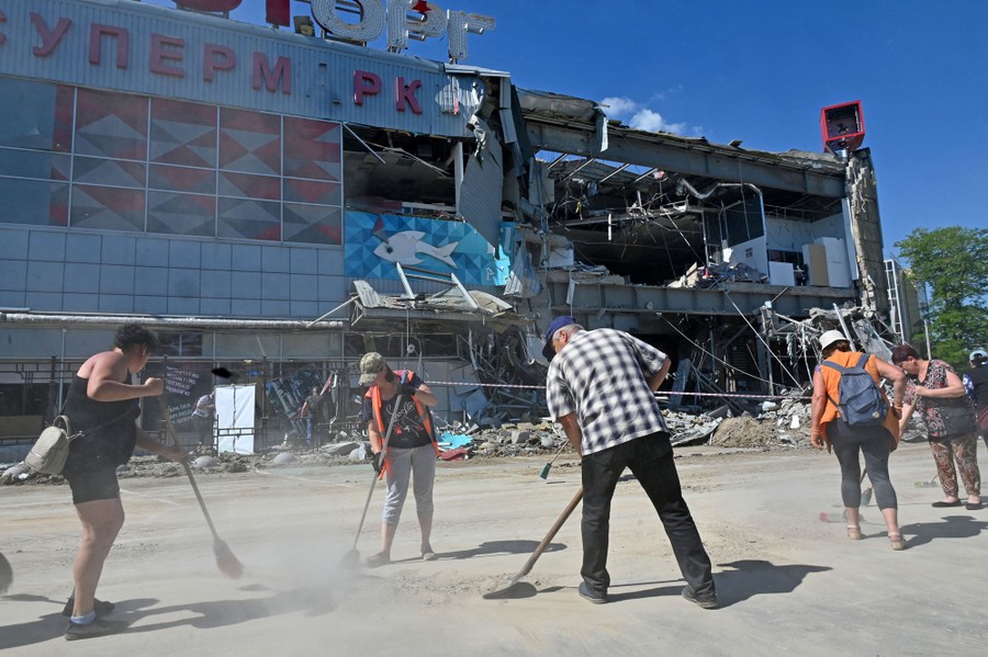 A half-dozen people sweep dust and debris outside a bombed supermarket.