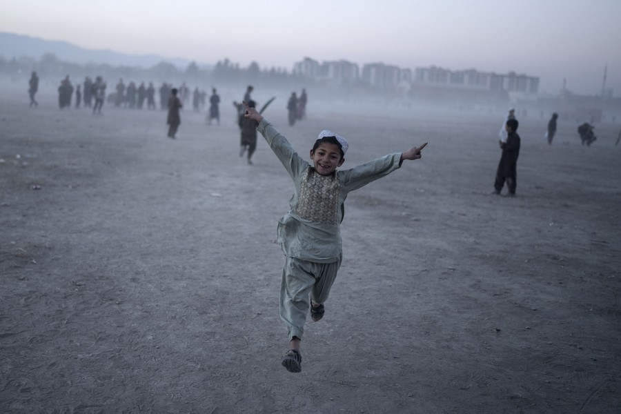 A young boy celebrates as he plays cricket on a dusty field.
